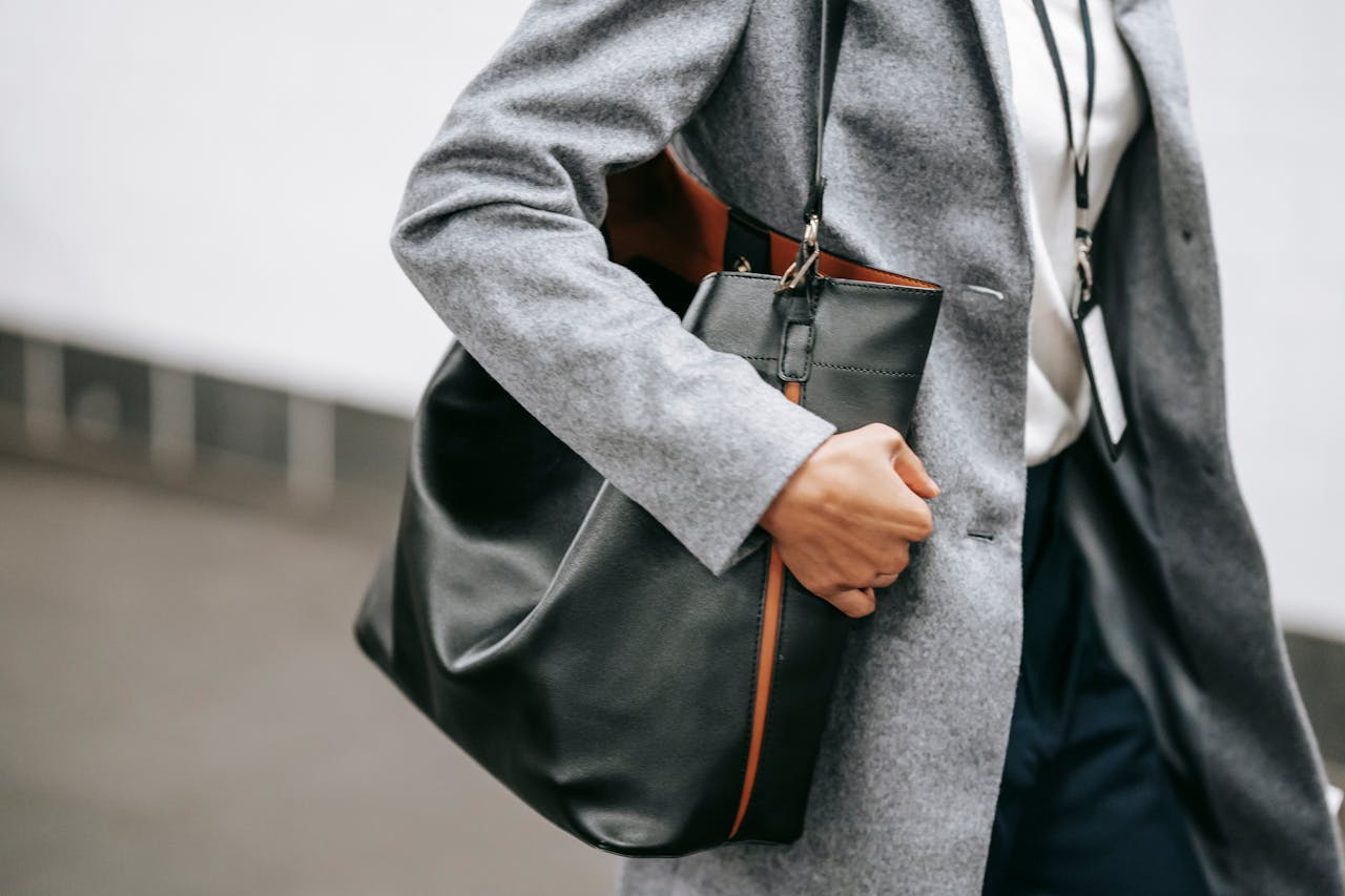 Elegant businesswoman in a gray coat holding a leather bag, walking outdoors.